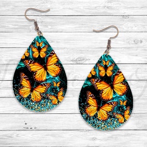 May include: A pair of teardrop-shaped earrings with a turquoise and black background. The earrings are decorated with multiple orange and yellow butterflies.