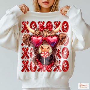 May include: White sweatshirt with a red and white graphic of a cow wearing heart-shaped sunglasses and a red bow tie. The cow is holding a red lollipop. The graphic is surrounded by red XOXO text.