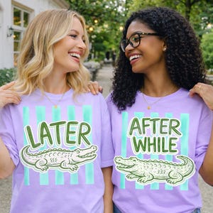 May include: Two women wearing matching lavender t-shirts with a green and white alligator graphic. One shirt says "LATER" and the other says "AFTER WHILE" in green text. The shirts have vertical teal stripes.