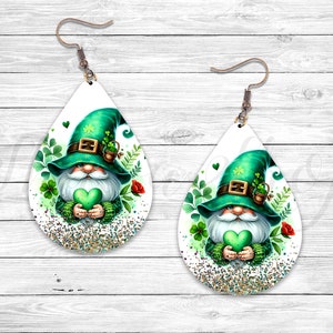 May include: A pair of white teardrop-shaped earrings with a green glitter background. Each earring features a cartoon gnome wearing a green hat with a shamrock and holding a green heart.