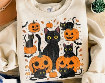 Op de afbeelding: Een crèmekleurige sweater met ronde hals en een grafische print van meerdere zwarte katten en oranje pompoenen. Het ontwerp bevat kleine vleermuizen, herfstbladeren en paddenstoelen verspreid rond de katten en pompoenen.