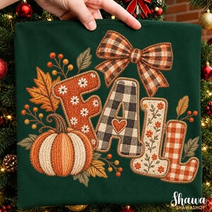 May include: A dark green shirt featuring an embroidered design with the word FALL in large letters. The letters are decorated with orange floral patterns, black and white buffalo plaid, and a small heart. A pumpkin and plaid bow are included.
