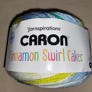 May include: A ball of Caron Cinnamon Swirl Cakes yarn. The label reads "Caron Cinnamon Swirl Cakes" in colorful text. The yarn itself is a mix of blue, green, yellow, and white.