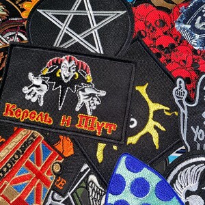 May include: A collection of embroidered fabric patches featuring various designs including a white pentagram on a black circle, a jester figure with the text "Король и Шут" in red and yellow, a red double-decker bus with a Union Jack, and blue polka dots.