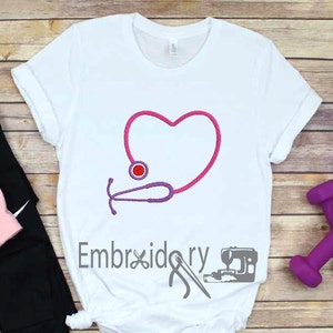 May include: White t-shirt with an embroidered design of a pink heart with a purple stethoscope wrapped around it. The stethoscope has a red circle at the end.