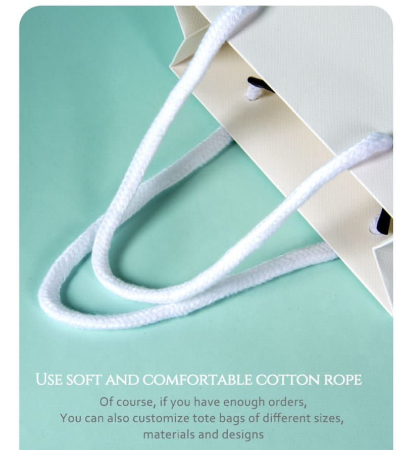 May include: Close-up of a cream-colored paper tote bag with white cotton rope handles. The bag has a textured surface and is set against a light teal background. Text on the image reads: "USE SOFT AND COMFORTABLE COTTON ROPE."