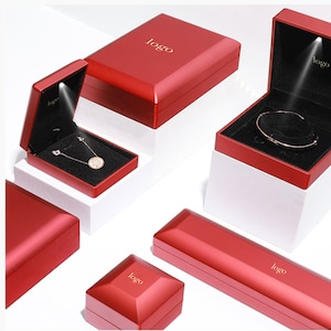 May include: Red jewelry boxes with a glossy finish, some open to reveal jewelry. The boxes have a black interior and a small light. The word "logo" is printed on the top of each box. A necklace and bracelet are visible inside the boxes.