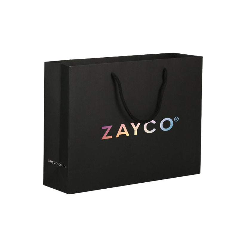 May include: Black shopping bag with a rectangular shape and a black rope handle. The bag features the word "ZAYCO" in a rainbow holographic font. The website address "zayco.com" is printed in white on the lower left corner.