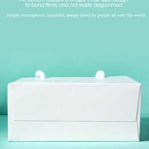 May include: A white gift box with two white rope handles. The box has a textured surface and the text "The bottom adopts a unique cross-type design to bond firmly and not easily degummed. Simple, atmospheric, beautiful, deeply loved by people all over the world."