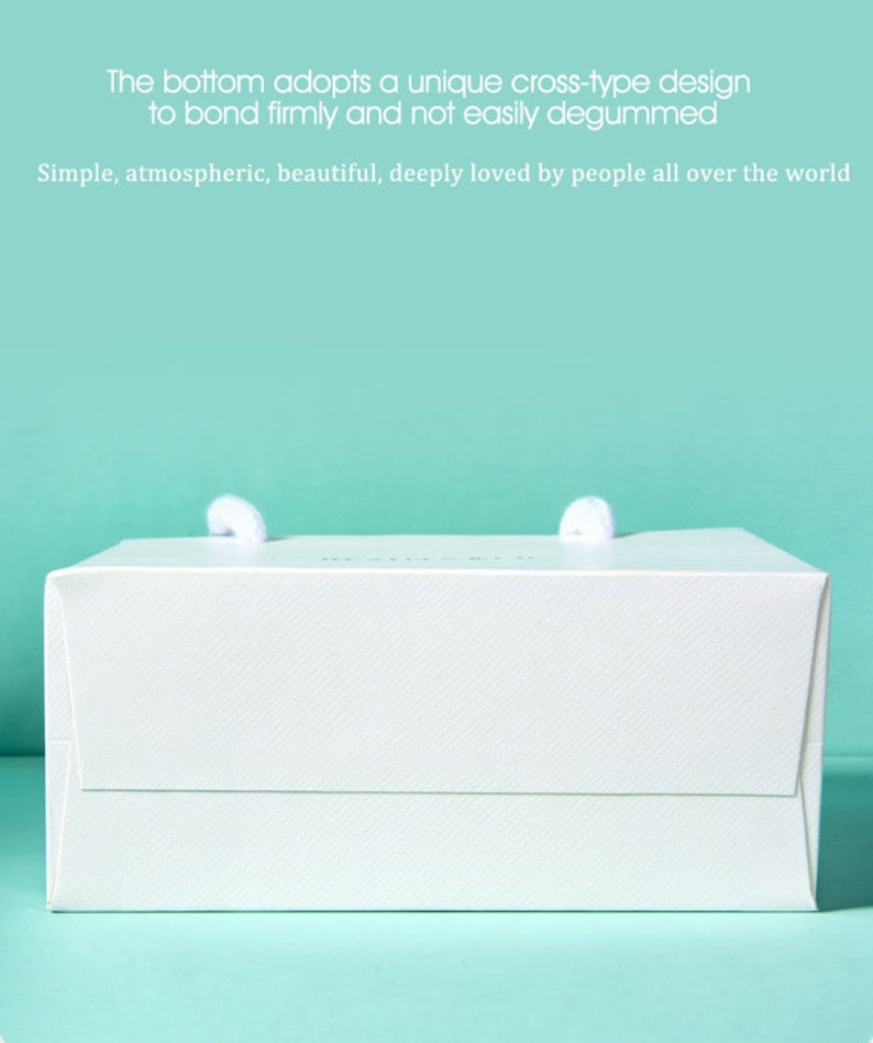 May include: A white gift box with two white rope handles. The box has a textured surface and the text "The bottom adopts a unique cross-type design to bond firmly and not easily degummed. Simple, atmospheric, beautiful, deeply loved by people all over the world."
