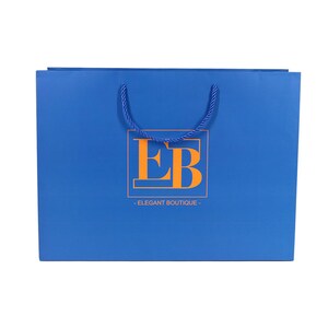 May include: A blue shopping bag with a rope handle. The bag features the orange letters "EB" inside a rectangular frame, with the words "ELEGANT BOUTIQUE" below.