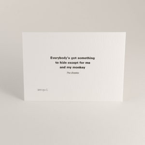 以下が含まれることがあります： 白いカードに黒い文字で「Everybody's got something to hide except for me and my monkey.」と書かれています。テキストの下には「The Beatles」と印刷されています。カードには「George E.」の署名があります。