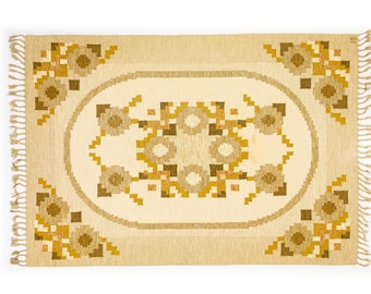 May include: A beige rug with a brown and yellow geometric pattern. The rug has a fringe border.
