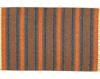May include: A striped rug with orange and blue stripes. The rug has a fringe border.