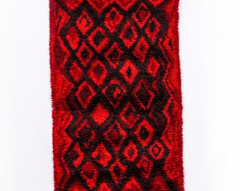 May include: A red and black geometric patterned rug with a fuzzy texture.