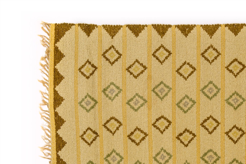 May include: A beige rug with a geometric pattern of brown and green diamonds. The rug has a fringe border.