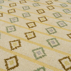 May include: A white rug with a geometric pattern of brown, yellow, and green diamonds. The pattern is repeated throughout the rug.