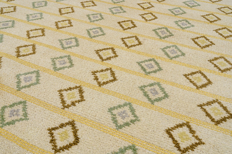 May include: A white rug with a geometric pattern of brown, yellow, and green diamonds. The pattern is repeated throughout the rug.