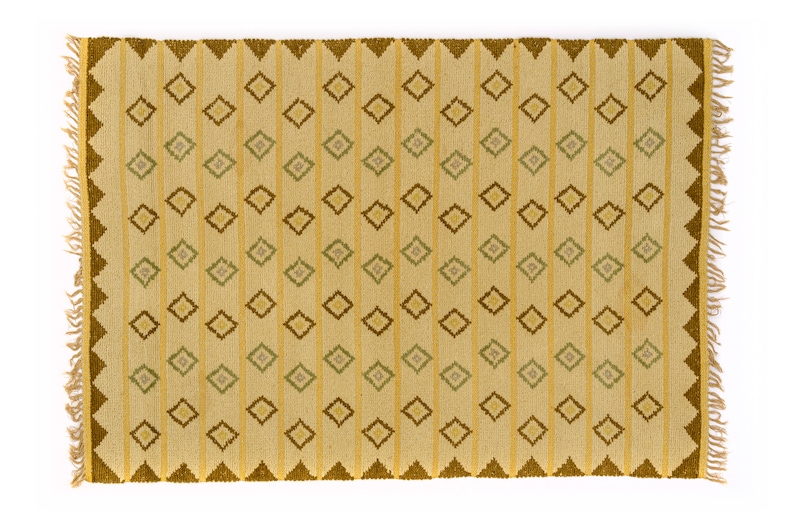May include: A beige rug with a geometric pattern of brown, yellow, and green diamonds. The rug has a fringe border.