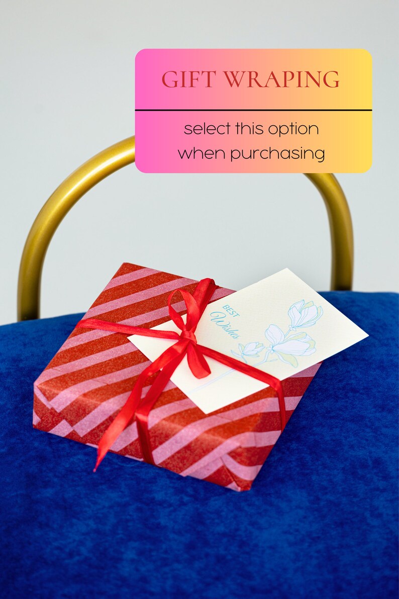May include: A red and pink striped gift box with a red ribbon and a white card that says "Best Wishes" with a blue flower illustration. The box is sitting on a blue surface.