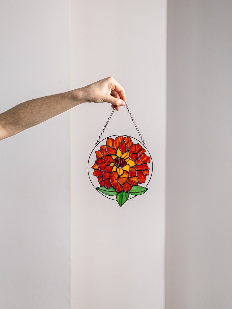 May include: A stained glass window hanging with a red, orange, and yellow flower design with green leaves.