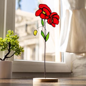 May include: A stained glass poppy flower sculpture with red petals and green leaves on a wooden base.