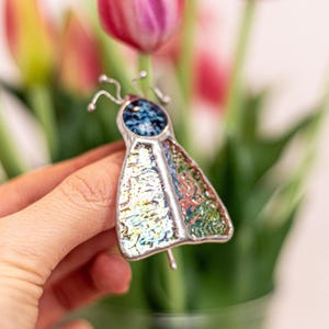 May include: A stained glass butterfly with iridescent wings and a blue center. The butterfly is made of glass and metal and is a beautiful piece of art.