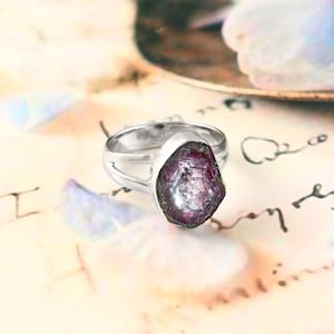 Könnte beinhalten: Eine weiße Keramik-Tasse mit schwarzem Henkel und dem Text "But First, Coffee" in fetter, schwarzer Schrift. Die Tasse steht vor einem verschwommenen Hintergrund, der eine gemütliche Umgebung suggeriert.