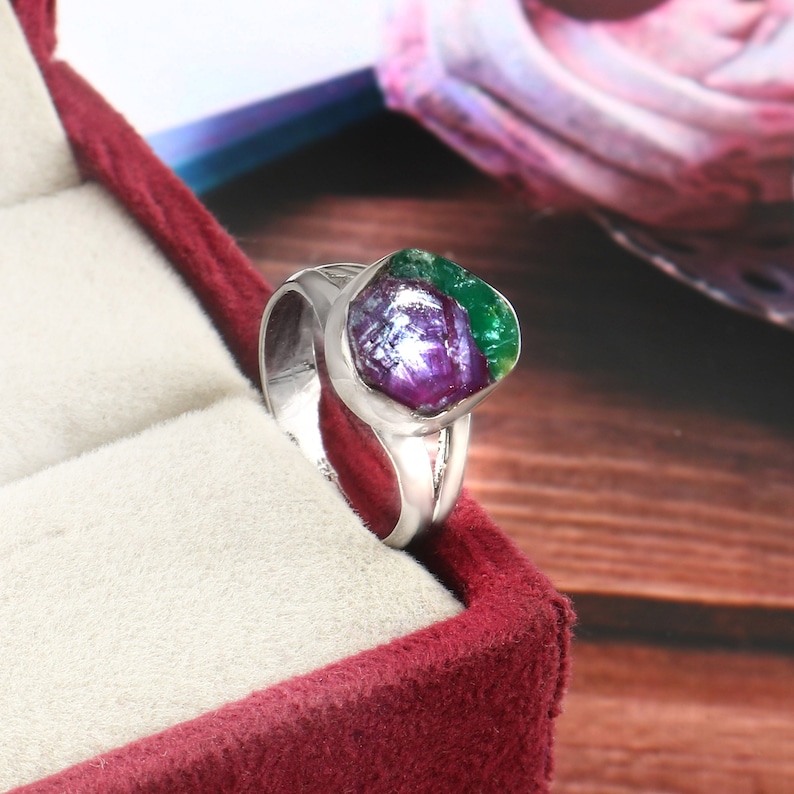 Pode incluir: Um anel de prata com uma pedra preciosa grande e irregular. A pedra exibe uma mistura vibrante de cores, incluindo roxo profundo, verde e toques de branco. O anel &eacute; definido em uma banda de prata polida.