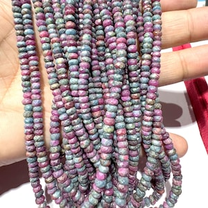 Może przedstawiać: Sznury fasetowanych koralików z kamieni szlachetnych w odcieniach różu, fioletu i szarości. Koraliki są małe i jednolitej wielkości, nawleczone, aby stworzyć naszyjnik lub bransoletkę. Kamienie szlachetne mają wypolerowaną, odblaskową powierzchnię.