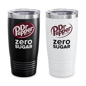 May include: Two insulated tumblers, one black and one white, each featuring the Dr Pepper logo and the words "zero sugar." The tumblers have a silver rim and a ridged design near the base. The Dr Pepper logo is in a burgundy color.