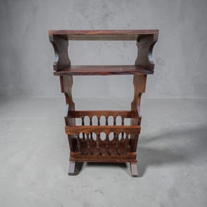 May include: A dark brown wooden magazine rack. It has two shelves and a decorative magazine holder at the bottom. The rack is supported by four short legs. The overall design is traditional and functional.
