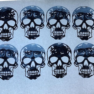 May include: A collection of twelve skull stickers. Each skull is black and white, with detailed facial features. The skulls are arranged in three rows of four, creating a repeating pattern.