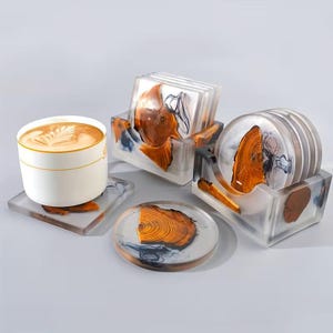 May include: A set of square and circular coasters made of clear resin with embedded natural wood slices and dark blue swirls. The set includes two matching resin holders and a white ceramic cup with latte art resting on one square coaster.