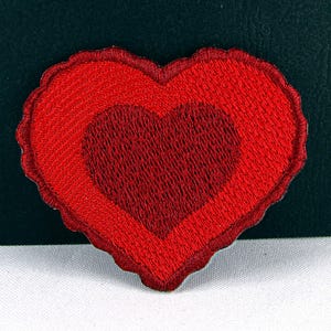 May include: Red felt heart-shaped patch with a smaller heart inside. The patch has a slightly textured surface.