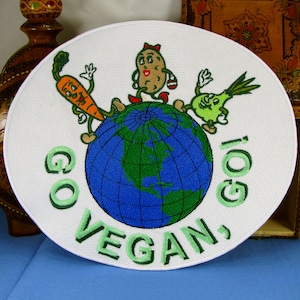 May include: White embroidered patch with a green, blue, and brown cartoon image of a potato, carrot, and onion standing on a globe. The text "GO VEGAN, GO!" is written in green around the globe.