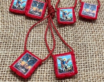 May include: Four square pendants on red cord necklaces, each featuring a small religious image. Two pendants display a depiction of a winged figure, and two pendants display a depiction of a crucifixion scene, all framed in red fabric borders.