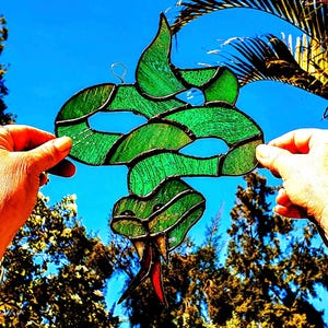 May include: A green stained glass snake with a red tail, held up against a blue sky.