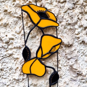 May include: Two yellow stained glass poppies with black outlines and gold accents on a white textured background.