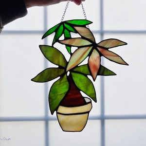 May include: A stained glass hanging of a potted plant with green and pink leaves. The plant is in a white pot with a brown base.