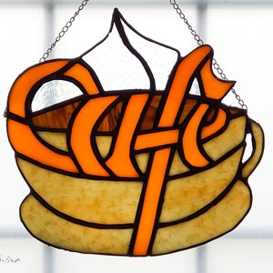 May include: A stained glass window hanging with a chain, depicting a coffee cup with the word "Cafe" in orange lettering.