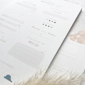 May include: A printable baby memory book with a light blue and white color scheme. The cover features a watercolor illustration of two bunnies hugging. The book includes sections for recording the baby's birthdate, time, weight, length, first words, and other milestones.