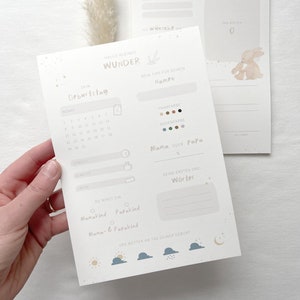 May include: A printable baby memory tracker with a light blue background and a cute bunny illustration. The tracker includes sections for the baby's birthday, hair and eye color, first words, and the weather on the day of their birth.