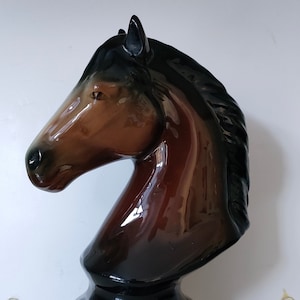 Puede incluir: Una figurita de cerámica de cabeza de caballo marrón y negro con un acabado brillante. La crin del caballo es negra y la base es negra.