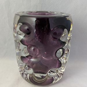 May include: A purple glass vase with a textured, bubble-like design. The vase is clear in some areas, revealing the purple glass inside.