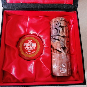 Könnte beinhalten: Ein rotes und goldenes Stempelkissen mit dem Text "E.P.I.R.E. YINNI" und ein roter und goldener geschnitzter Stempel aus Stein mit chinesischen Schriftzeichen.