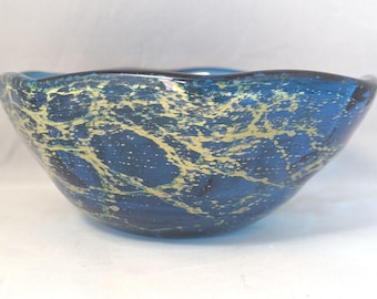 May include: A deep blue glass bowl featuring an irregular, web-like pattern of metallic gold flecks embedded within the material. The bowl has a smooth, rounded exterior surface and a wide, open top with a slightly undulating, curved rim edge.