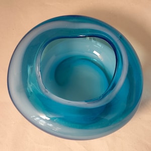 Pode incluir: Uma tigela de vidro azul com um design de redemoinho branco. A tigela é redonda e tem um acabamento liso e brilhante.