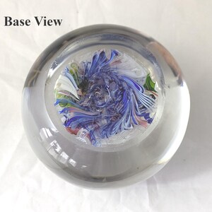 May include: A clear glass paperweight with a base view showing a swirling internal pattern of blue, white, green, and pink glass filaments. The text Base View is printed in black in the upper left corner of the image.
