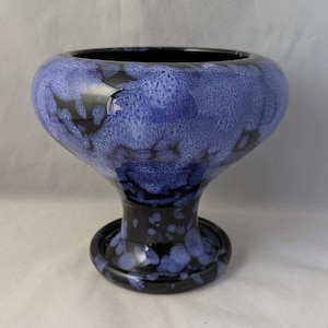 May include: A blue and black ceramic pedestal bowl with a speckled glaze. The bowl has a wide, round top and a narrow base.
